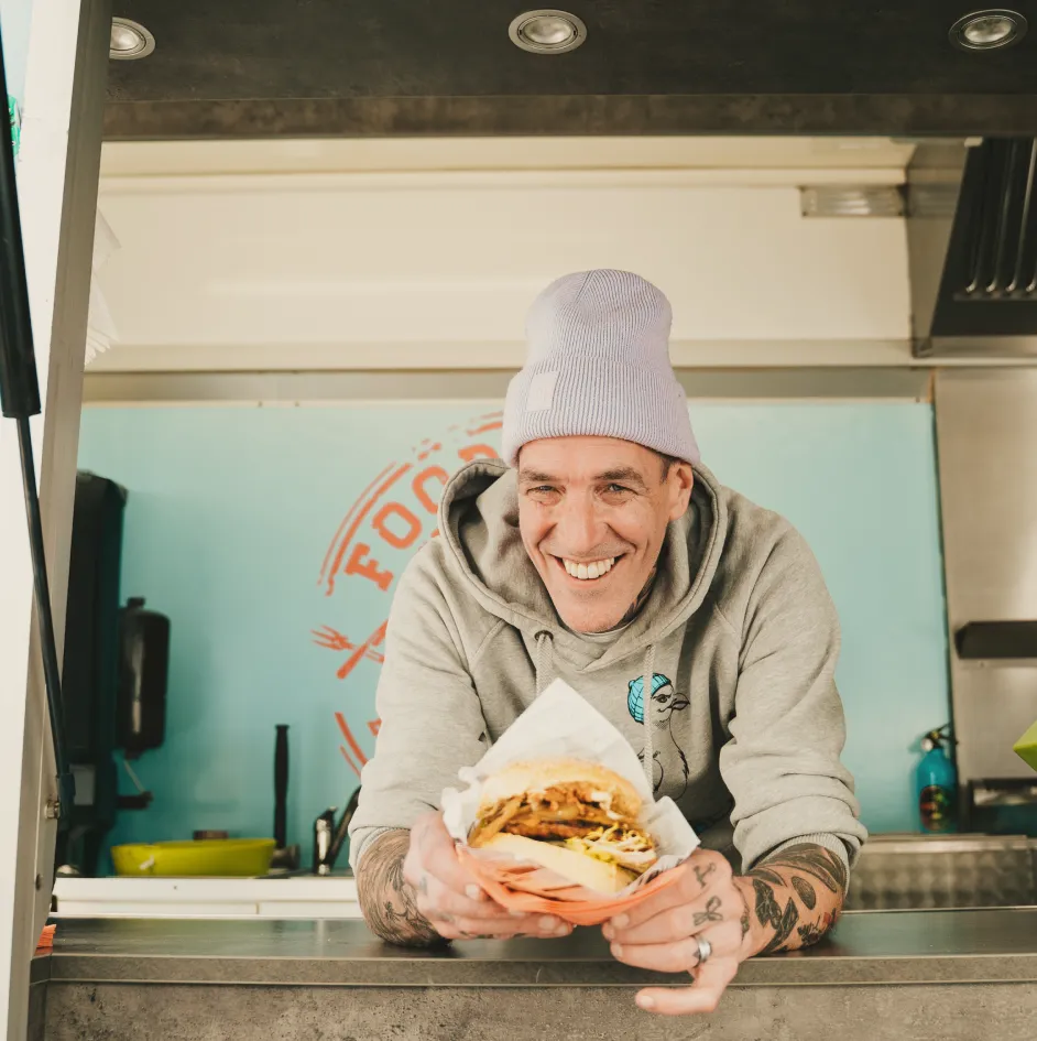 Bernd Müller, Gründer von Foodliner, präsentiert stolz einen frisch zubereiteten Burger in seinem Foodtruck – über 30 Jahre Erfahrung in der gehobenen Gastronomie.